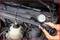 Measuring device shows pressure in the cooling system of a car. Hands holding the device, with the pressure in the red zone. Engine compartment in the background.