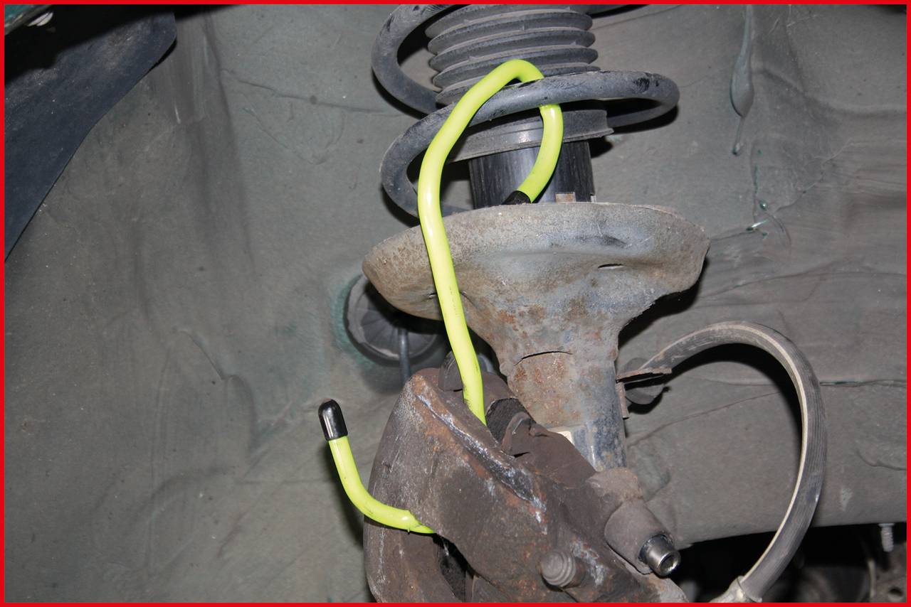 A yellow hose is wrapped around a rusty coil spring in a car. The hose is conspicuously and tightly wound around the spring.