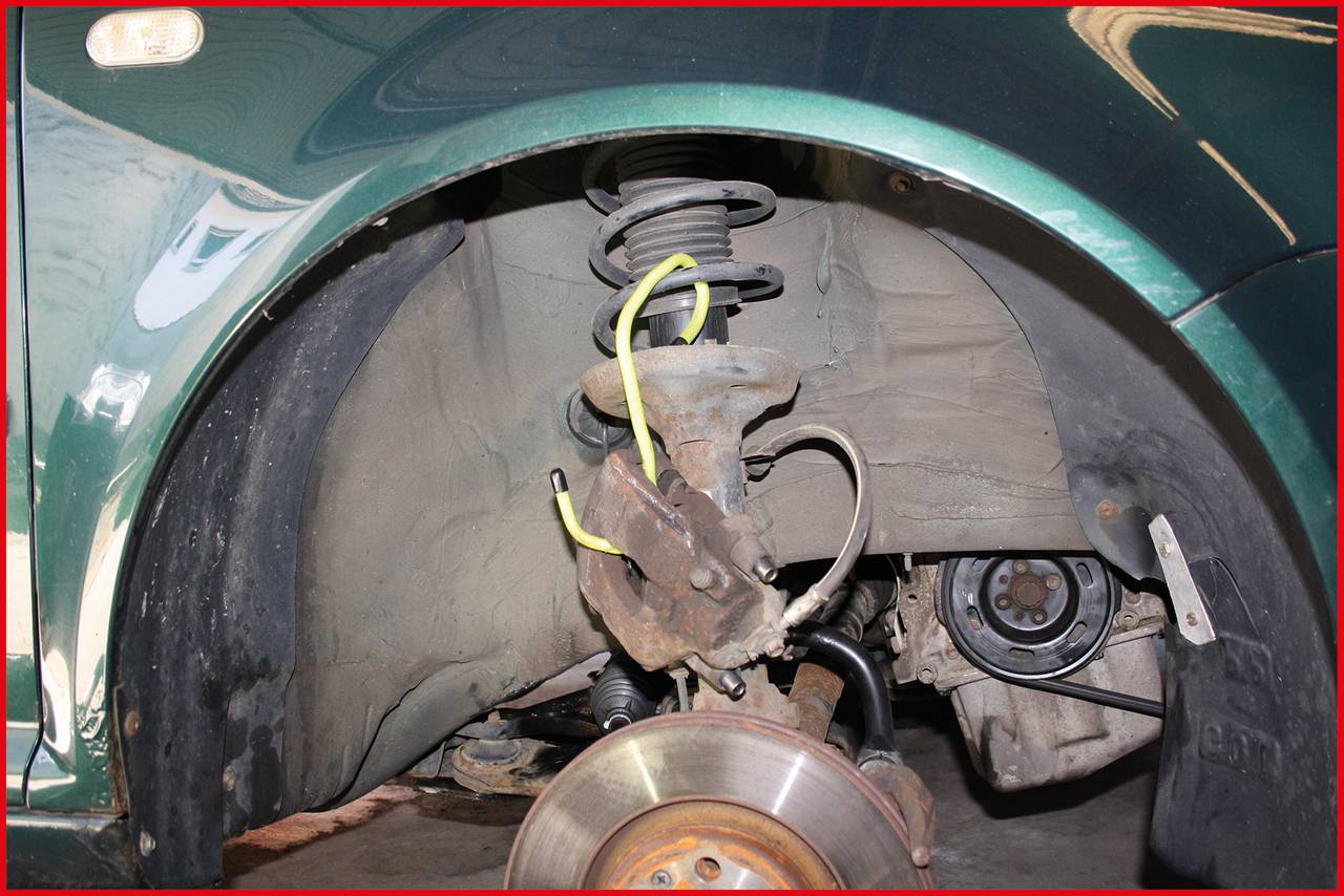 A car with a removed front wheel reveals the suspension and brake disc. Visible are the suspension strut, brake calliper, and brake disc.