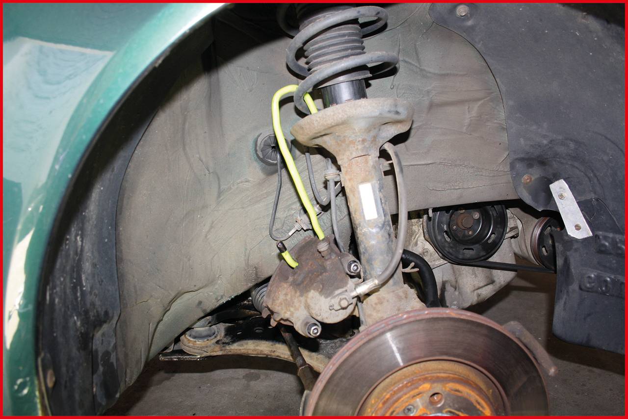 The front tyre of a car has been removed to reveal the suspension and brake components. A yellow pipe is visible.