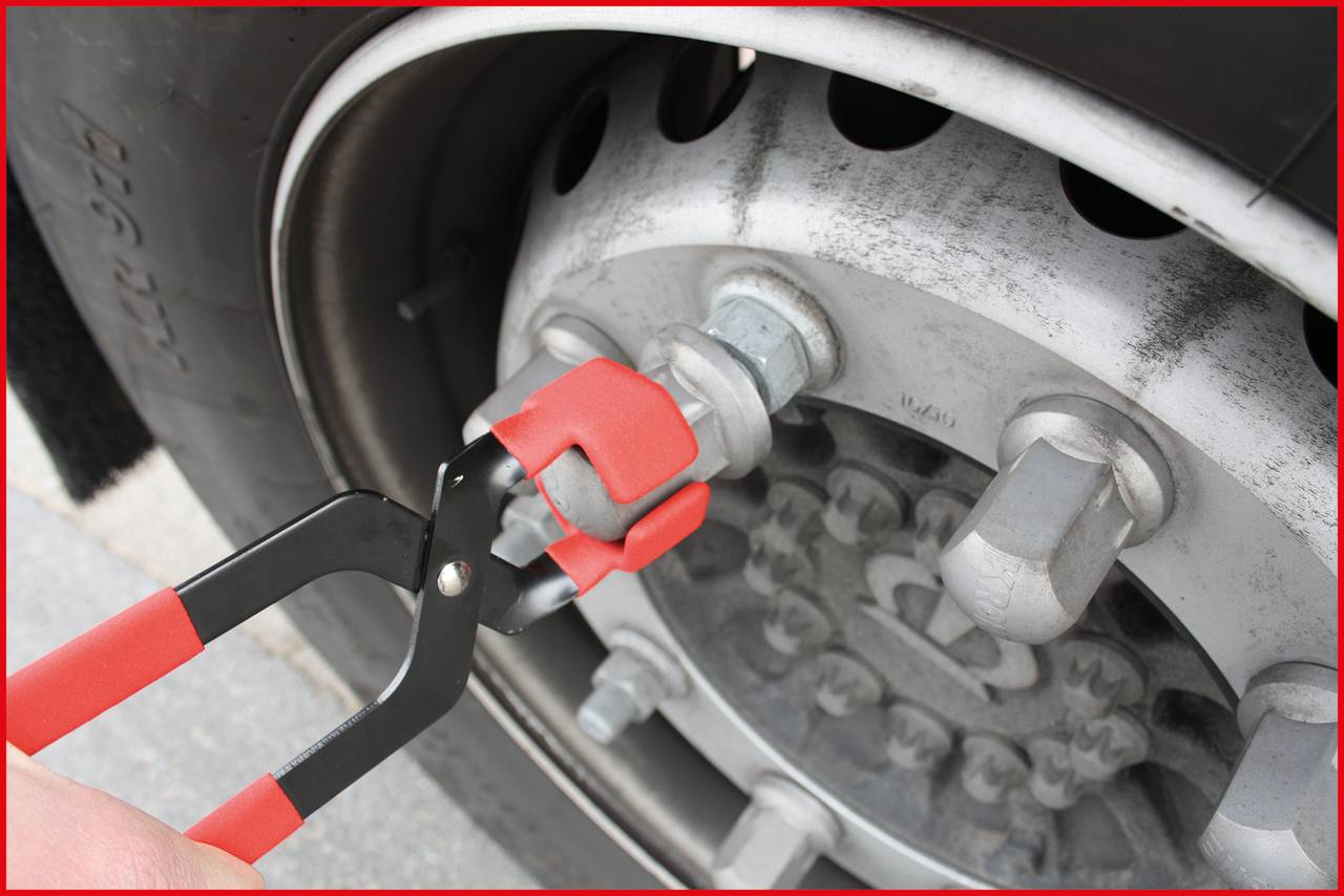 A person is using a red spanner to loosen a large nut on a lorry wheel.