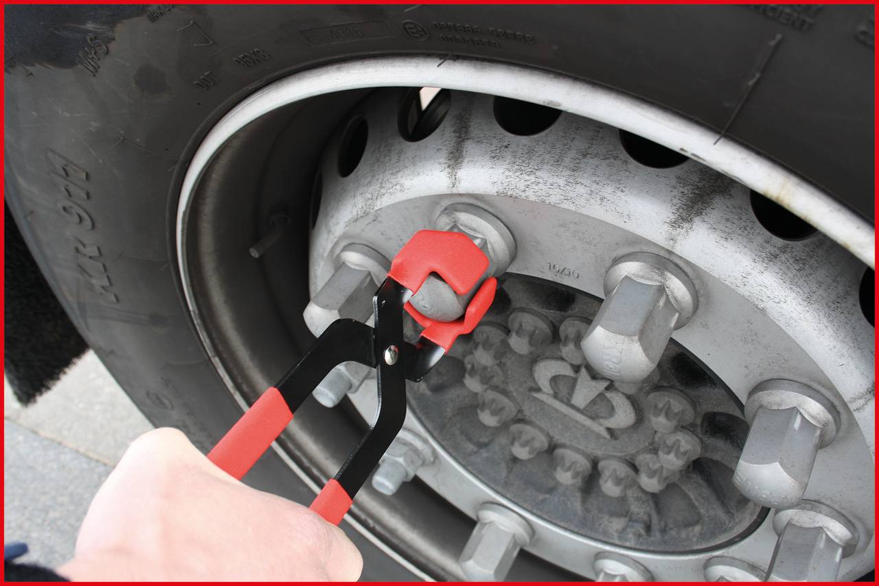 A hand is using a red spanner to loosen a wheel nut on a lorry tyre. The focus is on the tool and the wheel rim.