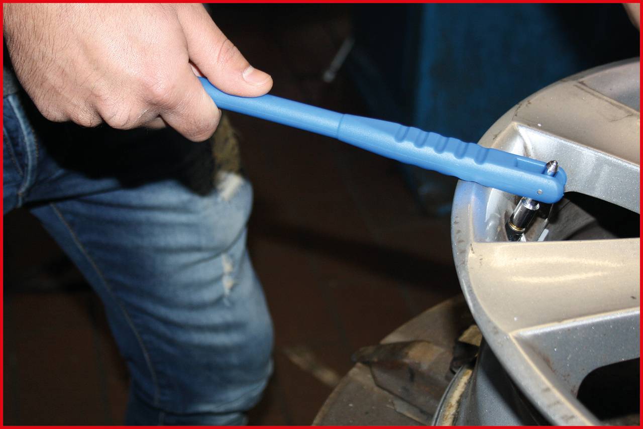 A person is tightening the screws on a car tyre with a blue spanner. The tyre is silver-coloured.