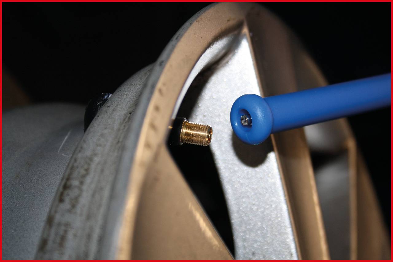 Close-up of a car tyre valve on a wheel, with a blue tool positioned against it. It appears that the tyre is being checked.