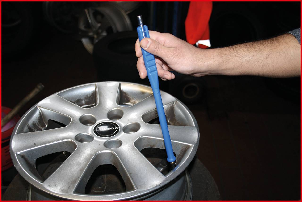 A hand is holding a blue pen, pointing at a silver car wheel.