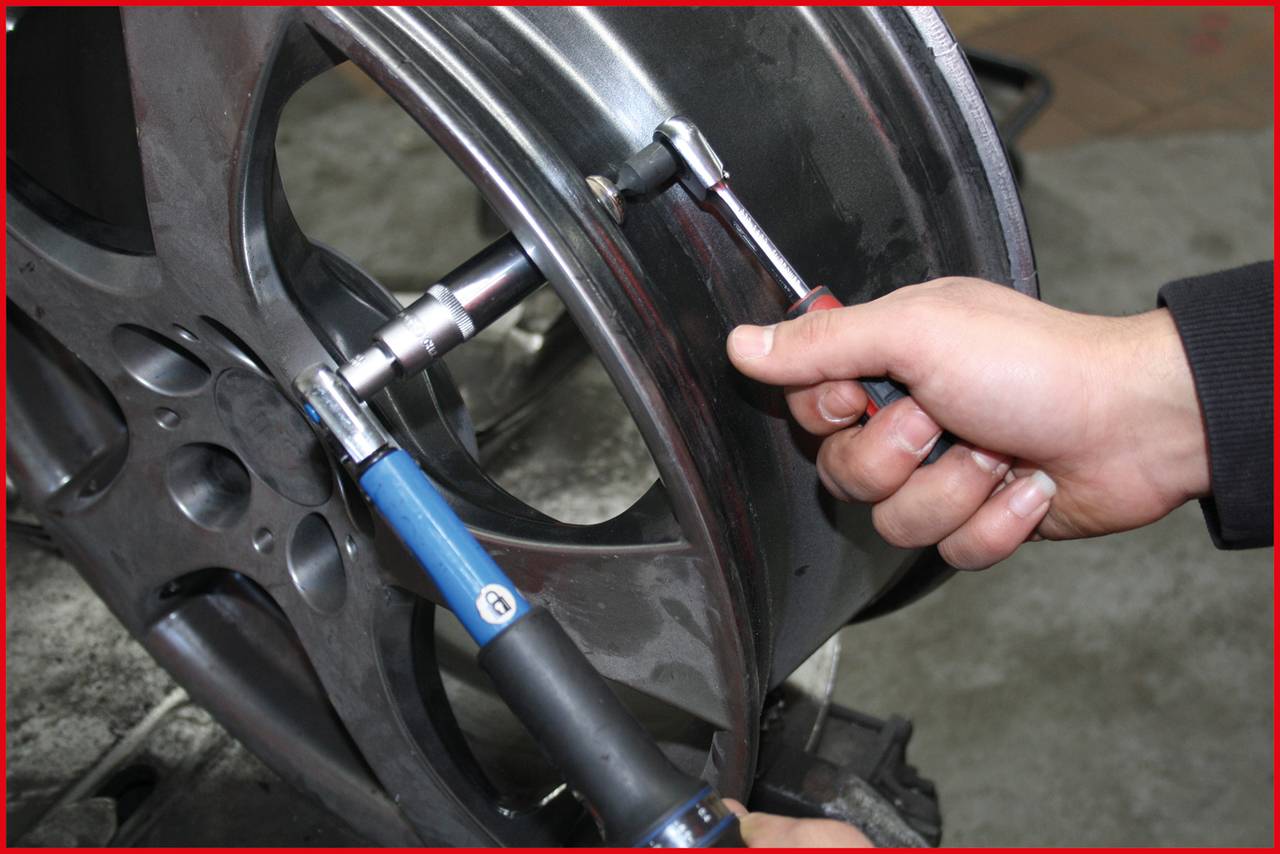 A person is repairing a car tyre wheel with tools in a workshop. Hands are visible working on the rim.