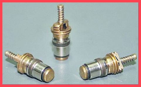 'Three metal valve cores on a table, varying in size and shape, against a neutral background.'