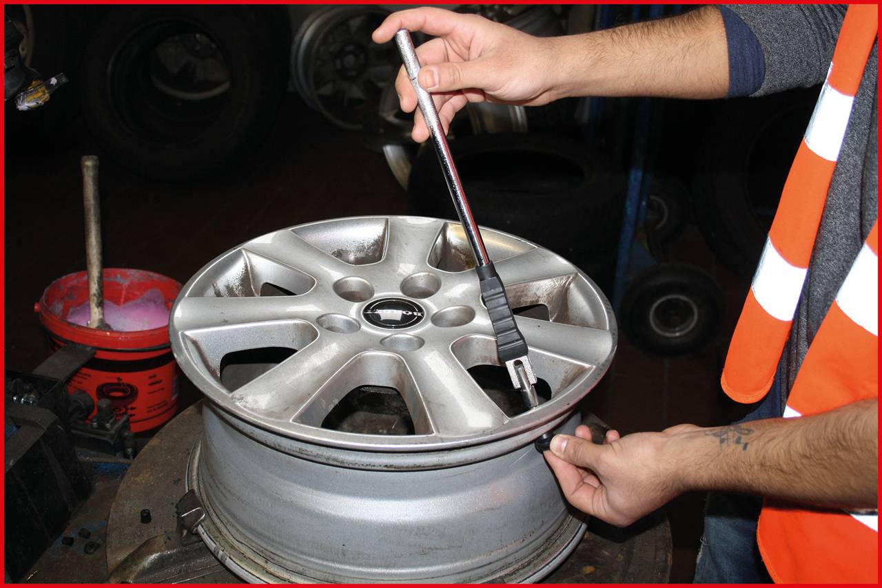A person is measuring the diameter of a car wheel rim with a measuring tool. The rim is resting on a workbench.