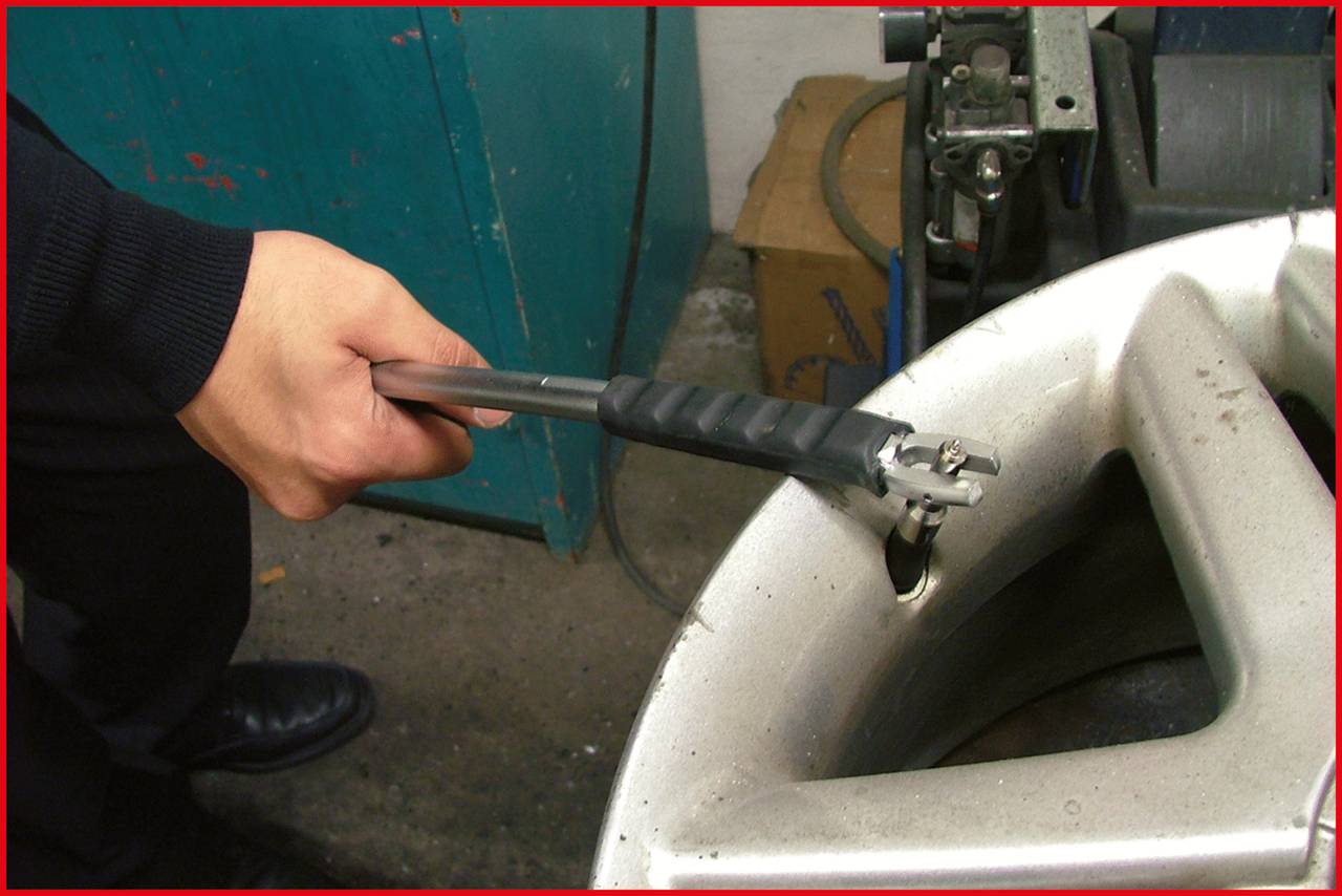 A person is checking the air pressure of a car tyre with a tyre pressure gauge in a workshop environment.