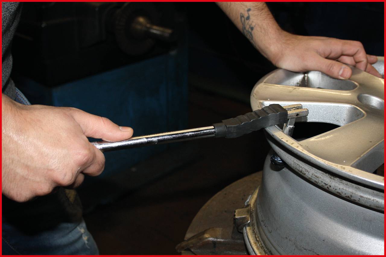 A person is checking the tyre pressure of a car alloy wheel in a workshop using a pressure gauge.