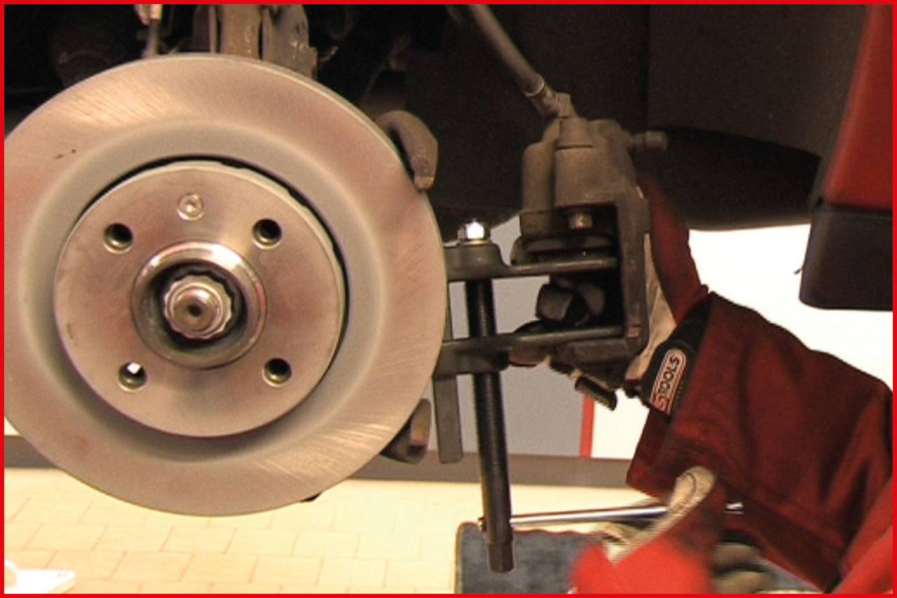 Close-up of a brake disc with brake pad on a vehicle wheel, mechanic's gloved hand adjusting components.