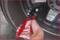 A hand grips a red tool handle, removing a wheel weight from a car tyre rim. A close-up emphasises the process of wheel balancing.