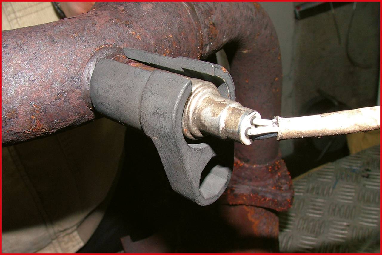 Close-up of a worn and rusted exhaust system with an oxygen sensor screwed into the pipe.