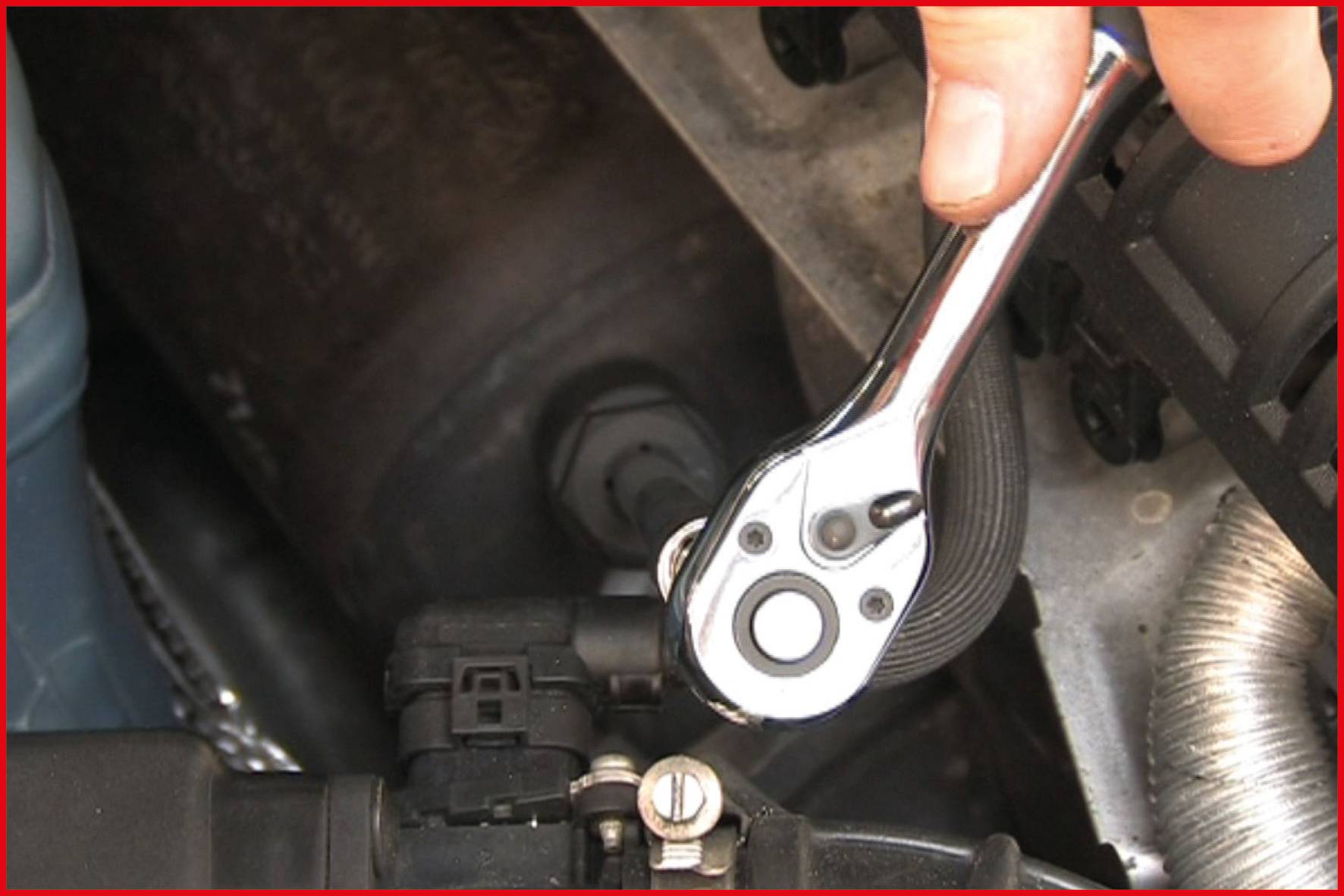A hand uses a ratchet spanner to tighten a screw on a car part in the engine bay.
