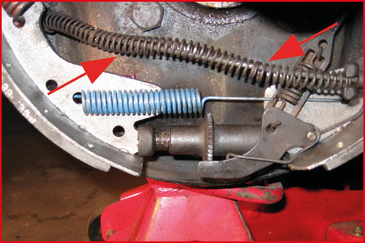 Brake drum of a vehicle brake with exposed springs and components, arrows pointing to specific parts for repair.
