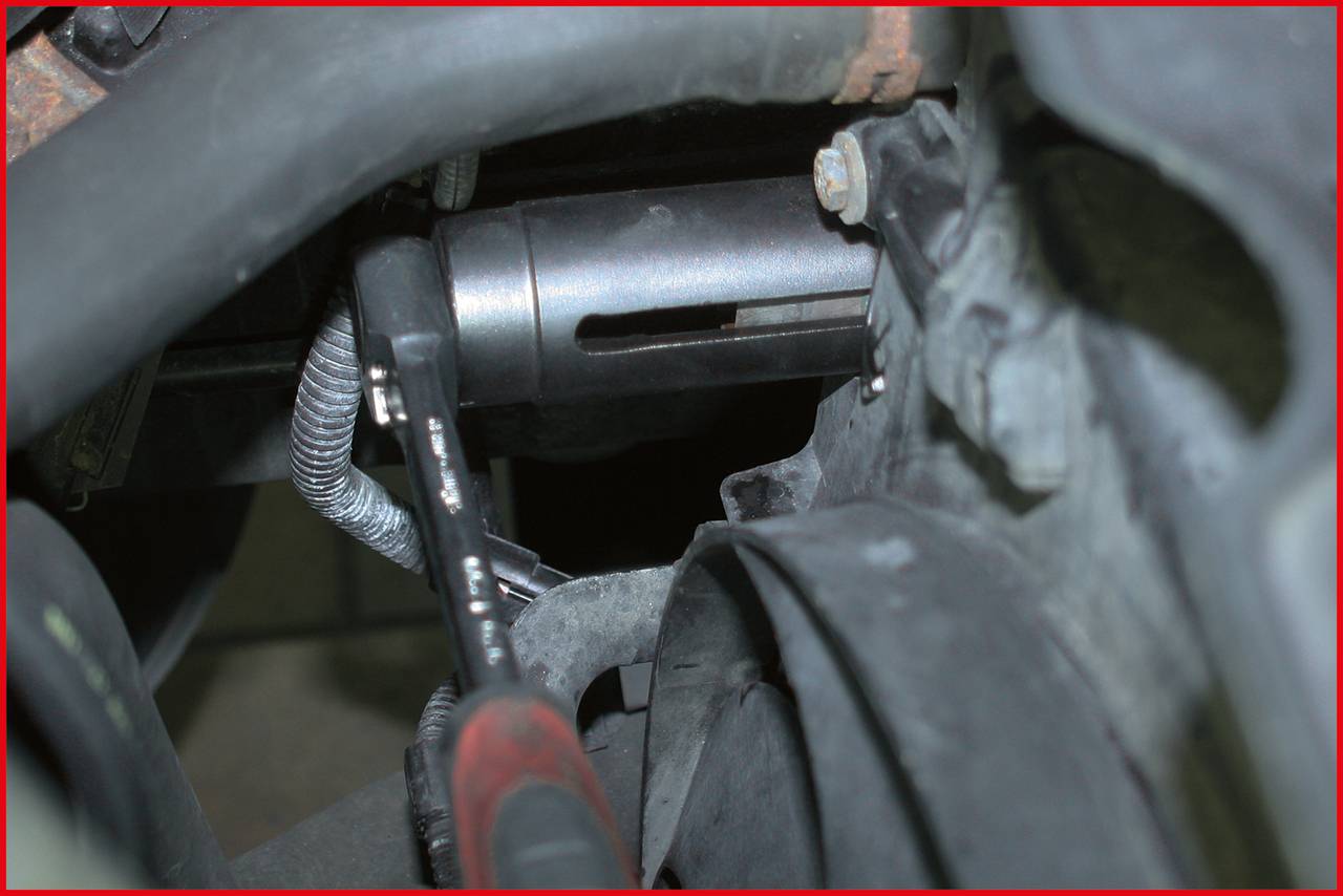 A mechanic's tool grips a round, metallic component in an engine bay. Repairs or adjustments are being carried out.
