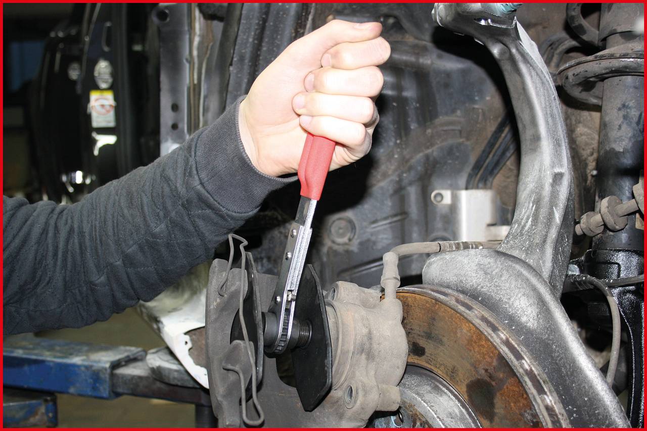 'A person is adjusting a bolt with a spanner on a car brake system to secure or release the brake disc.'