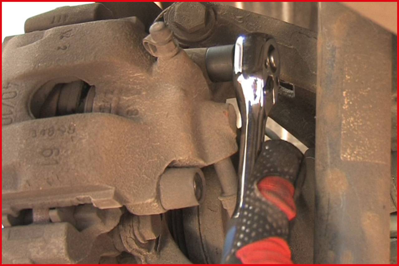 A mechanic uses a ratchet to work on a car brake calliper.