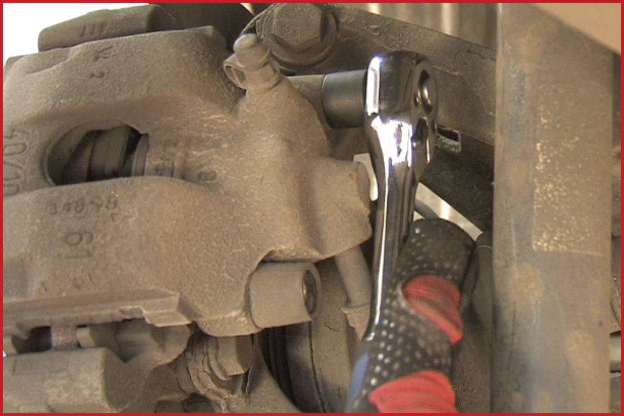 A spanner tightens a screw on a car brake system. The image focus is on the repair work.