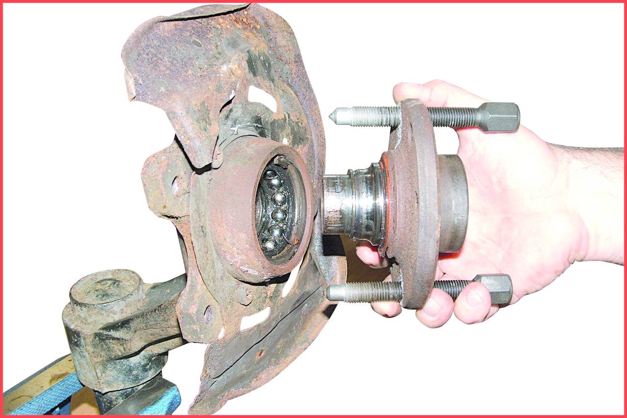 A hand is holding a rusty car wheel bearing next to a brake disc holder. The image depicts the removal or installation process of the bearing.