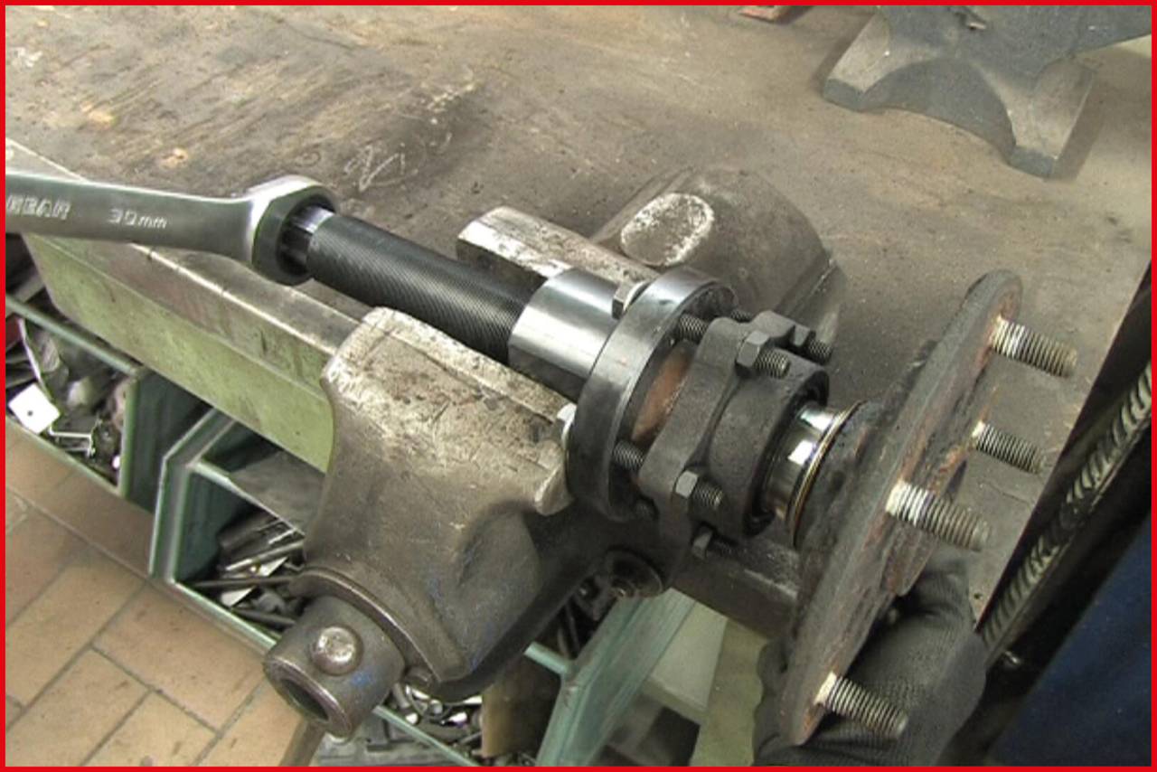 A workbench with a vice holds a car part. A spanner secures a bearing on the part. Several tools are scattered about.