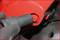 Close-up of a gloved hand attaching or loosening a black tool on a red mechanical component.