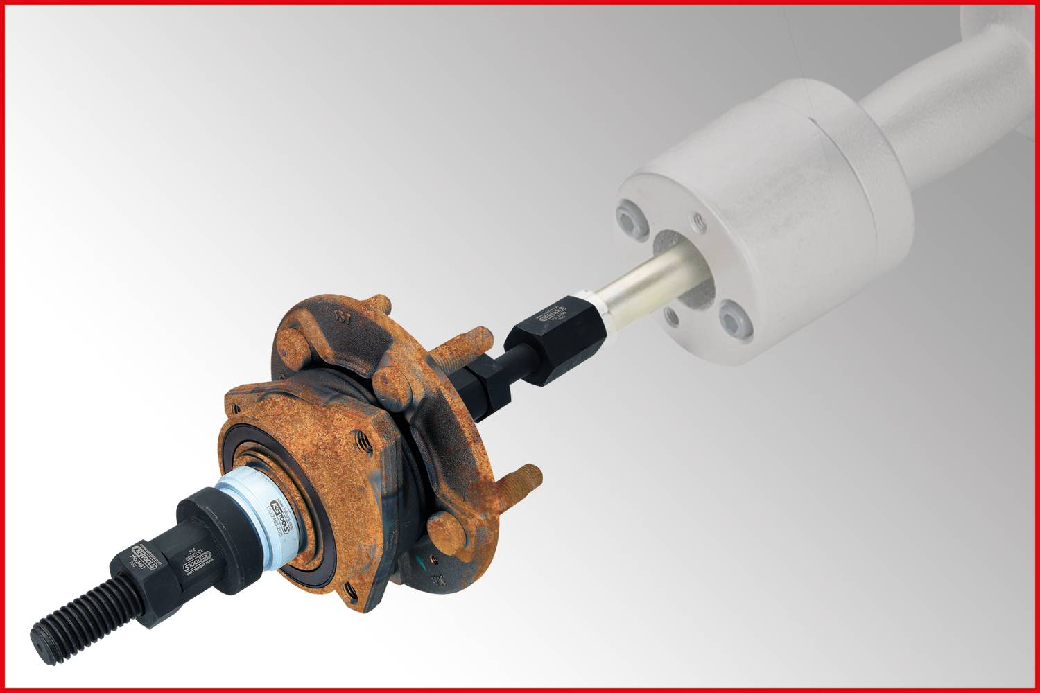 A tool is being inserted into a rusted wheel bearing set to pull the bearing out of the hub, against a grey background.