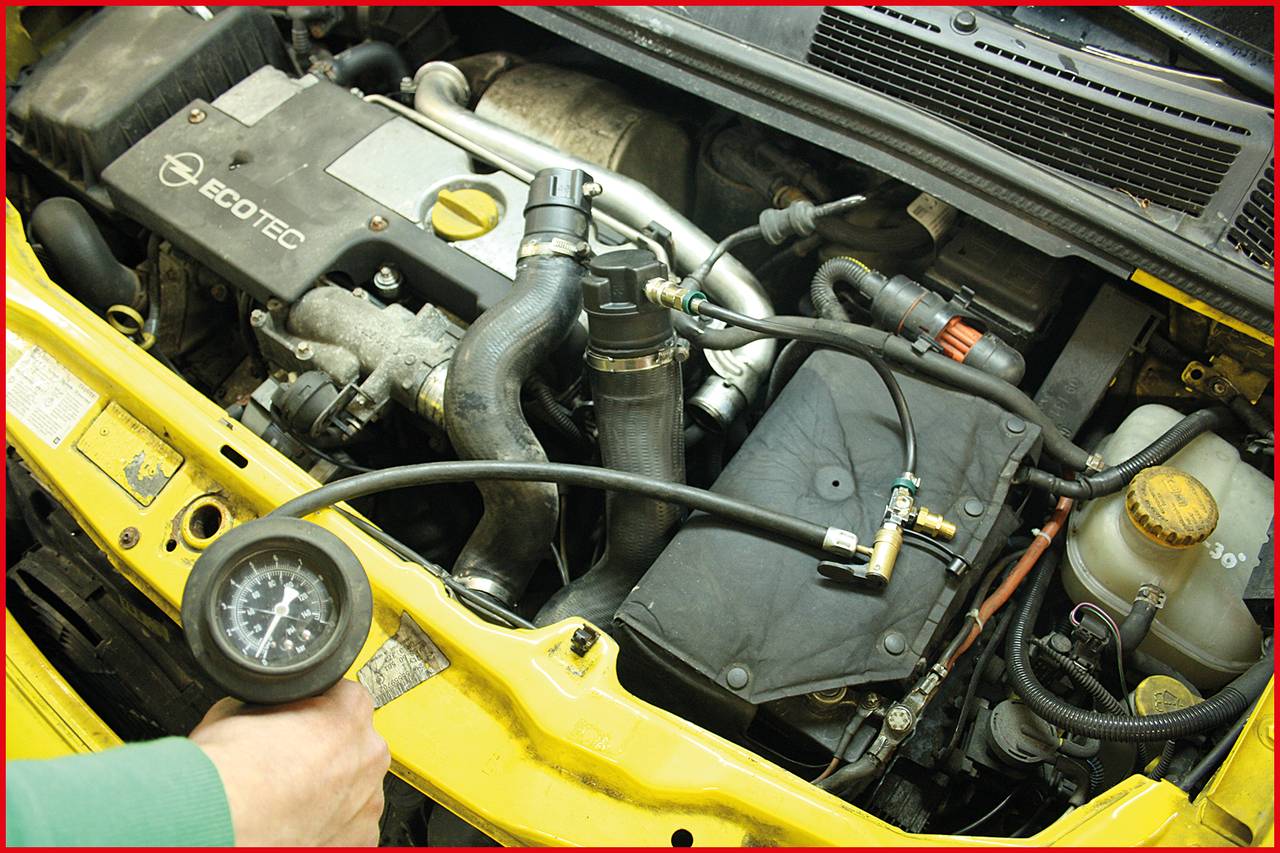 A mechanic is checking the engine compartment of a vehicle, specifically the hoses and connections, with a pressure gauge.