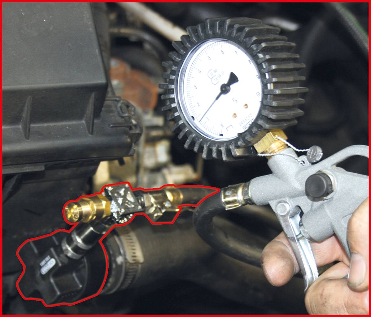 A person is holding a pressure gauge connected to a valve to check the pressure of an engine system.