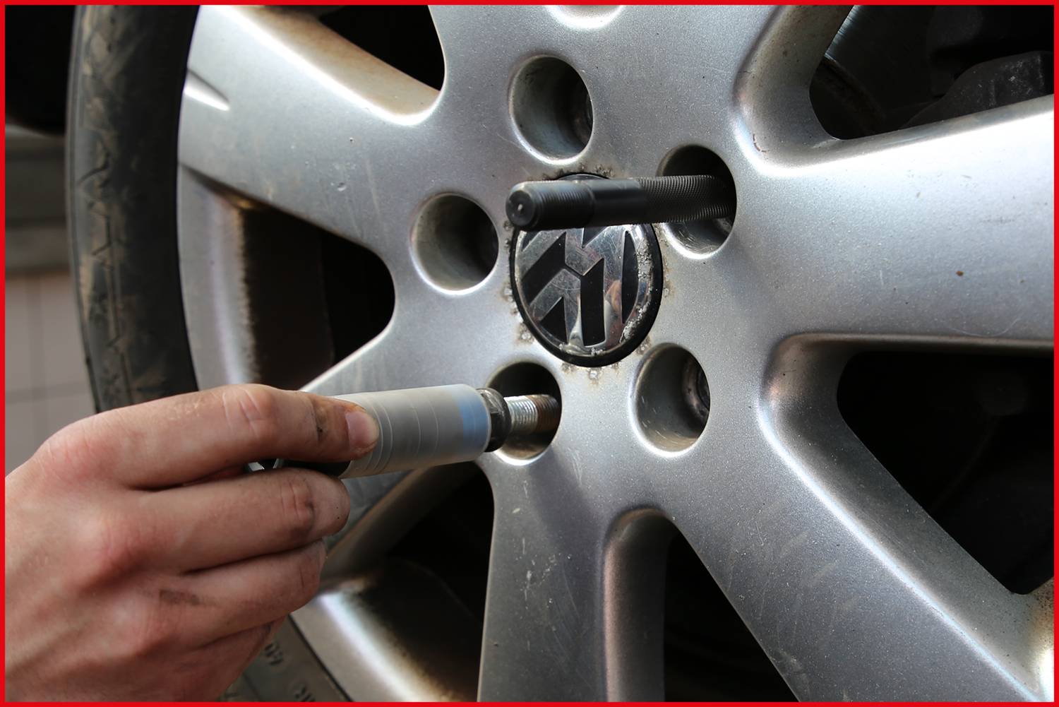 A hand tightens a wheel nut on a car tyre using a tool. The focus is on the wheel rim and the tool.
