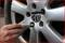 A hand tightens a wheel nut on a car tyre using a tool. The focus is on the wheel rim and the tool.