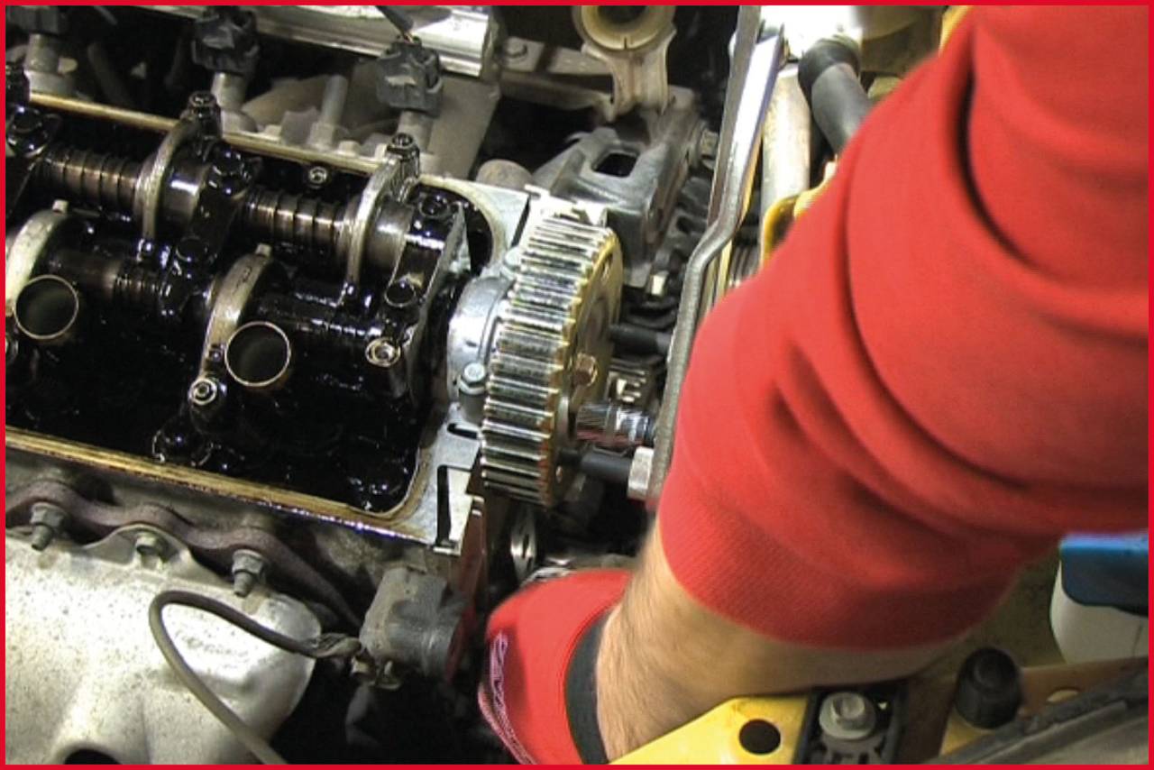 A mechanic in red clothing is repairing an exposed car engine. Gears and engine components are visible in close-up.