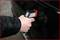 A hand is holding a portable device against a car door, which appears to be used for measuring temperature or thickness.