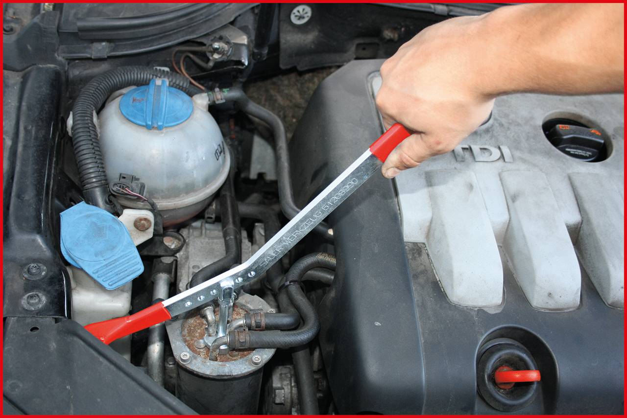 A hand is using a spanner to adjust a car part under the bonnet. A coolant reservoir is visible.