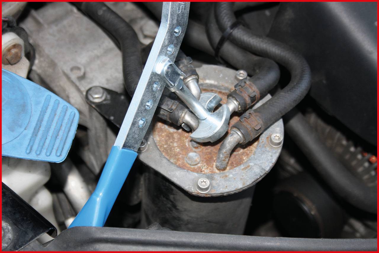 A spanner loosens or tightens a screw on a vehicle component with hoses. Possible context: Car repair.