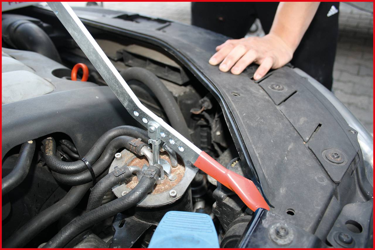 A person is working on a car and using a tool to open the bonnet. Hands are positioned on the vehicle frame.