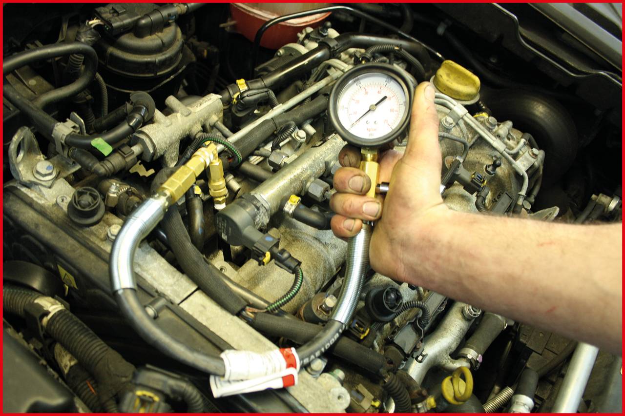 A hand is holding a pressure gauge over an engine to check the compression pressure. Hoses and engine parts are visible.