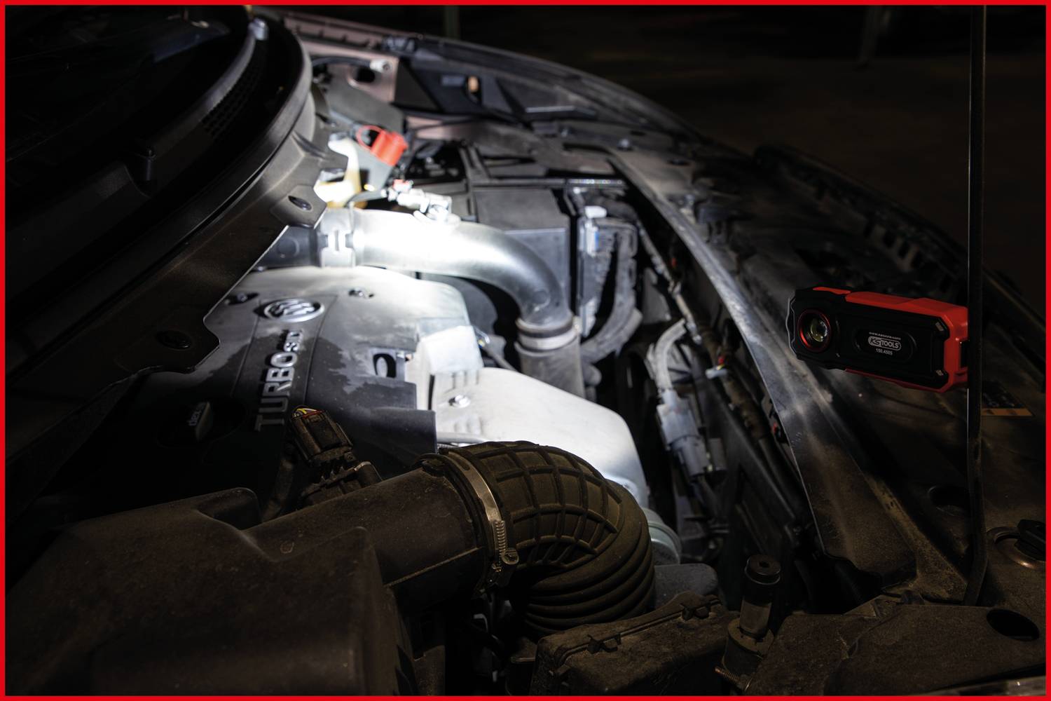 An open engine bay of a vehicle is illuminated, highlighting the 'Turbo' inscription on a component. A portable lamp lies beside it.