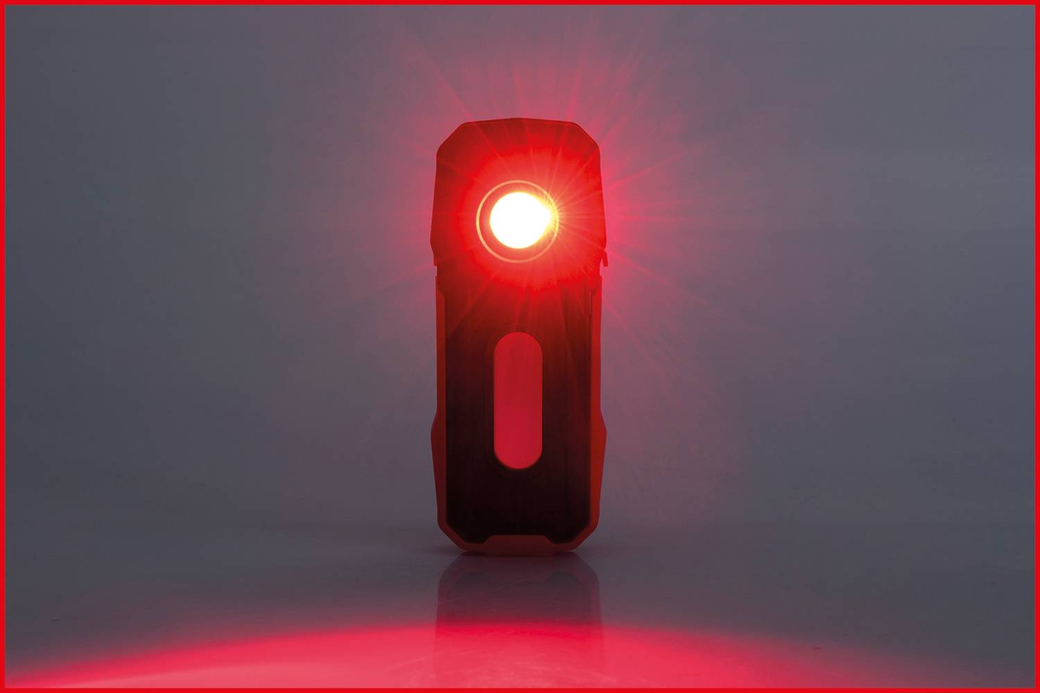 A black, standing device with a red light in the centre glows brightly on a grey surface.