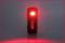 A black, standing device with a red light in the centre glows brightly on a grey surface.