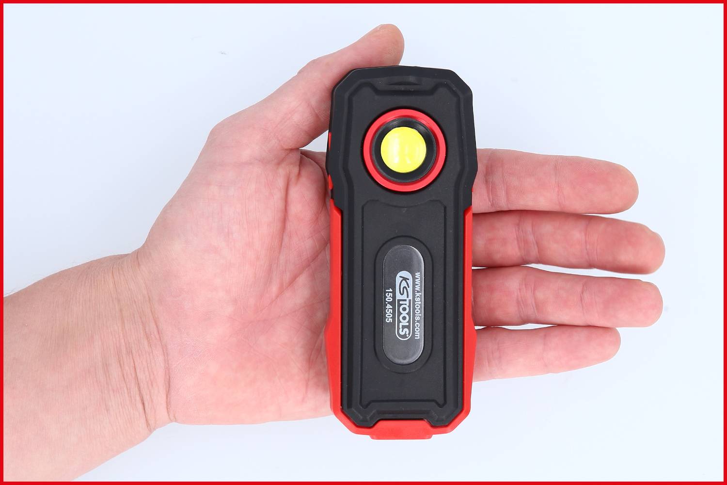 A rectangular red and black LED light device is being held in a hand. The light is switched off and displays the brand inscription.