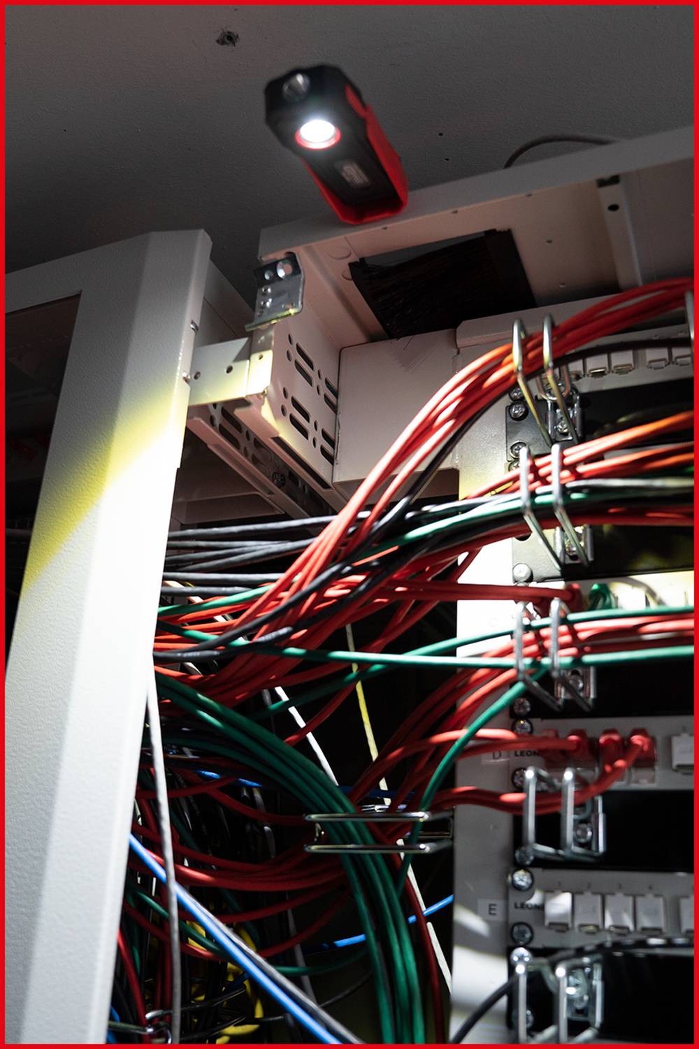 A network cabling cabinet with many coloured cables is illuminated. The cables are organised and connected to various sockets.