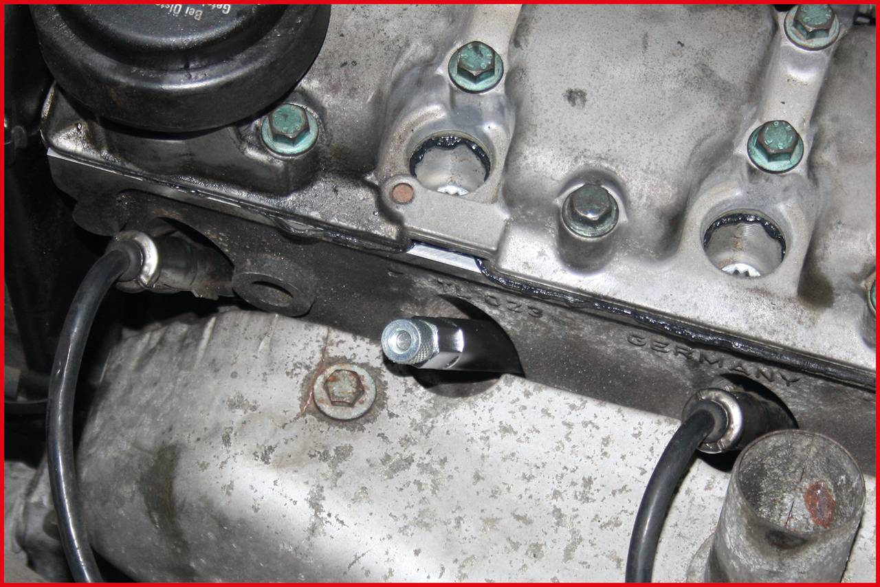 A car cylinder head with worn and corroded metal. Several bolts and cables are visible.