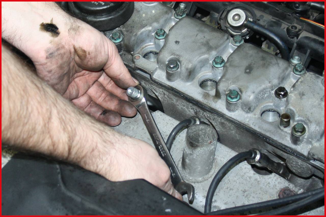 'Hands using a spanner are working on a car's engine.'