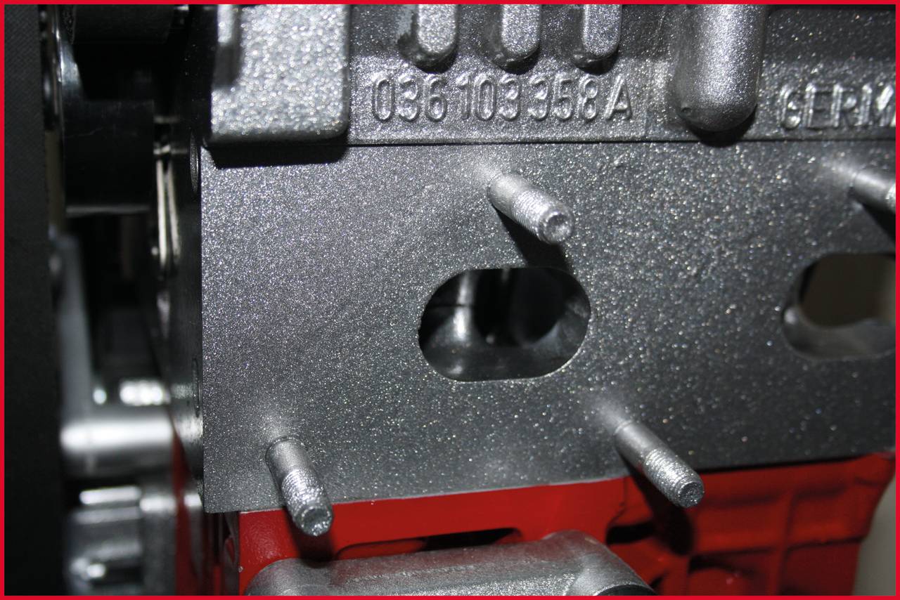 A metal block with several protruding bolts and a rectangular hole in the centre is shown in a close-up view.