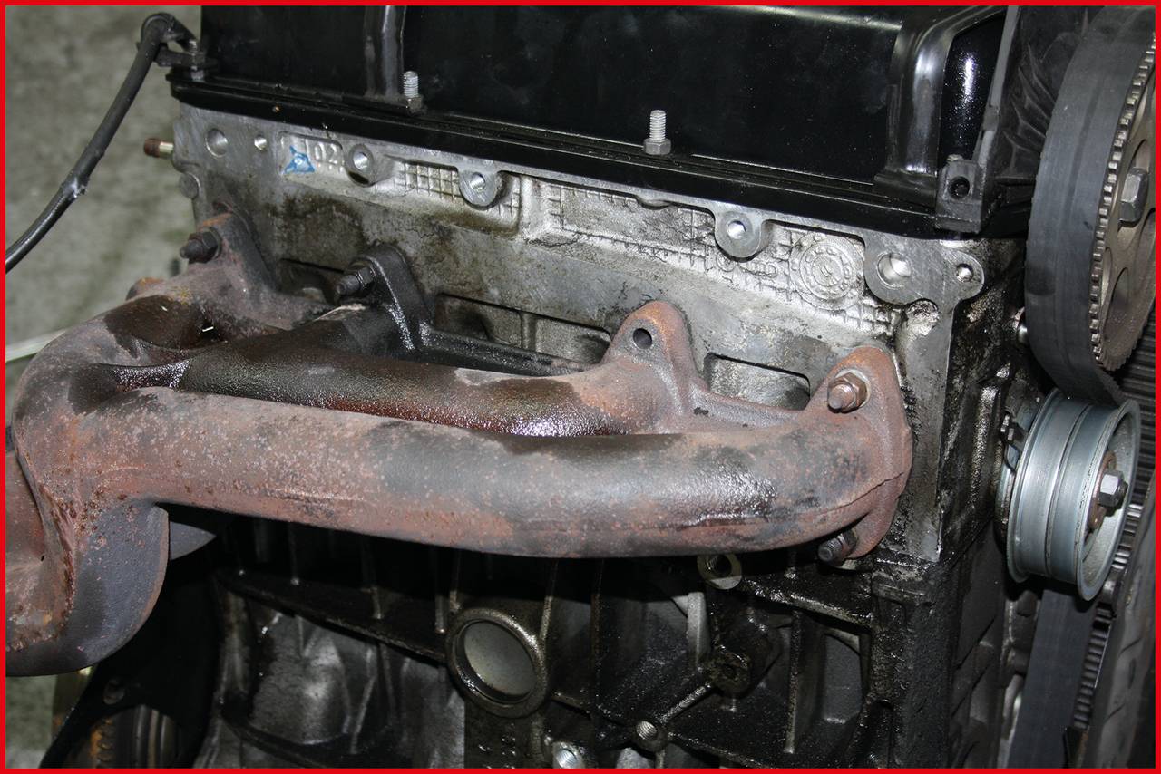'A rusted exhaust manifold on an engine block in a workshop environment.'