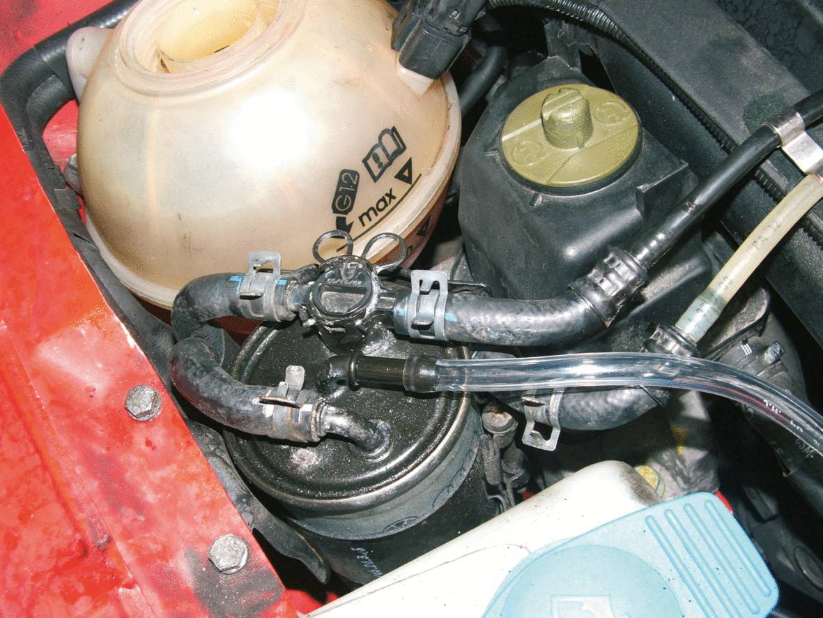 Engine compartment of a vehicle with a coolant reservoir and several hoses visible. Top right, a brake fluid container.