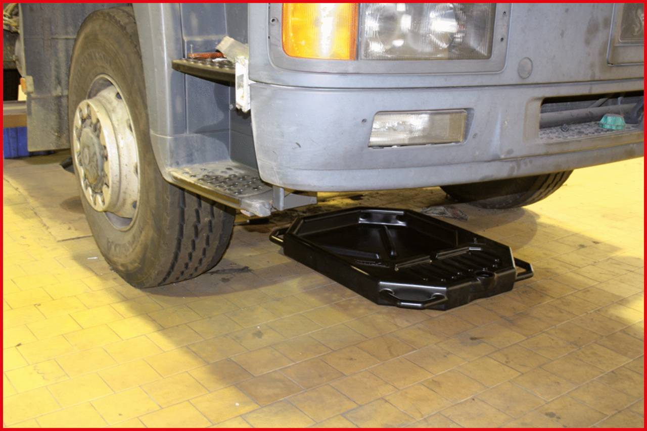 A lorry on a paved surface with a black drip tray positioned beneath the engine compartment.