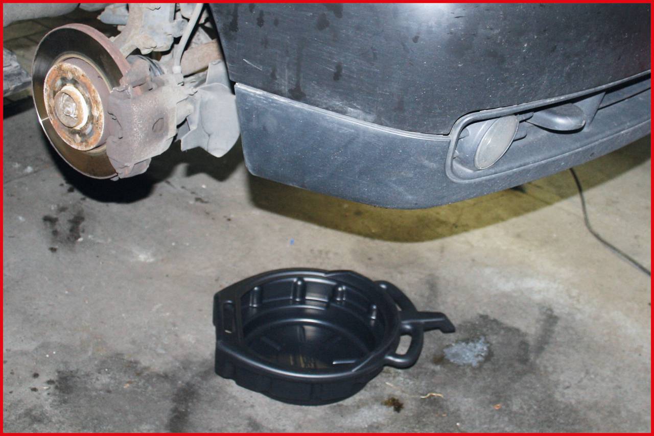 'A car jacked up for an oil drainage task. The front tyre is missing, and a black oil pan is positioned underneath to collect the draining oil.'