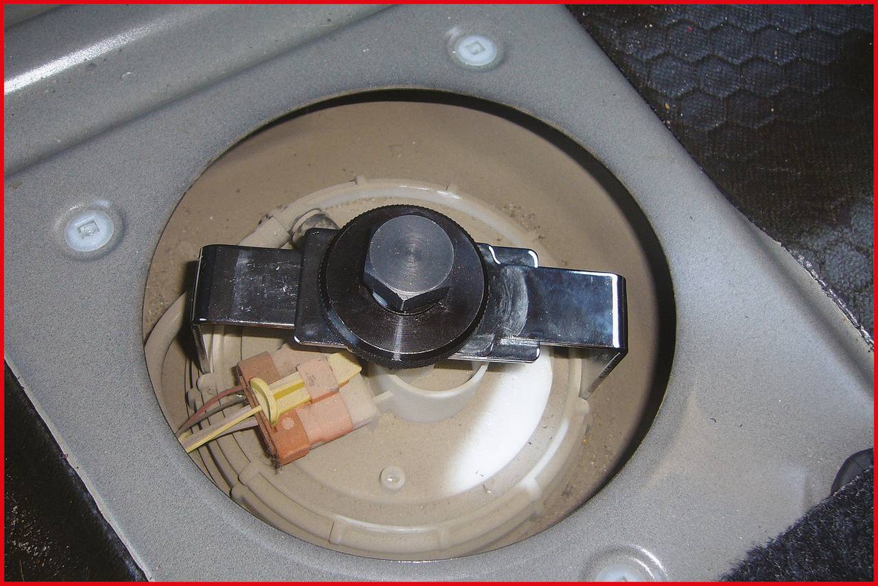 Car fuel filler cap opened, revealing electrical connections and metal mounting bracket inside.